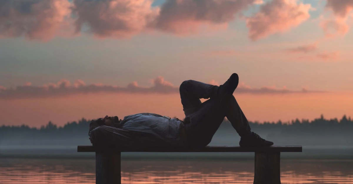 Rust is ook een werkwoord Man relaxing on a bench by a tranquil lake at sunrise, symbolizing rest, reflection, and mindful leadership.